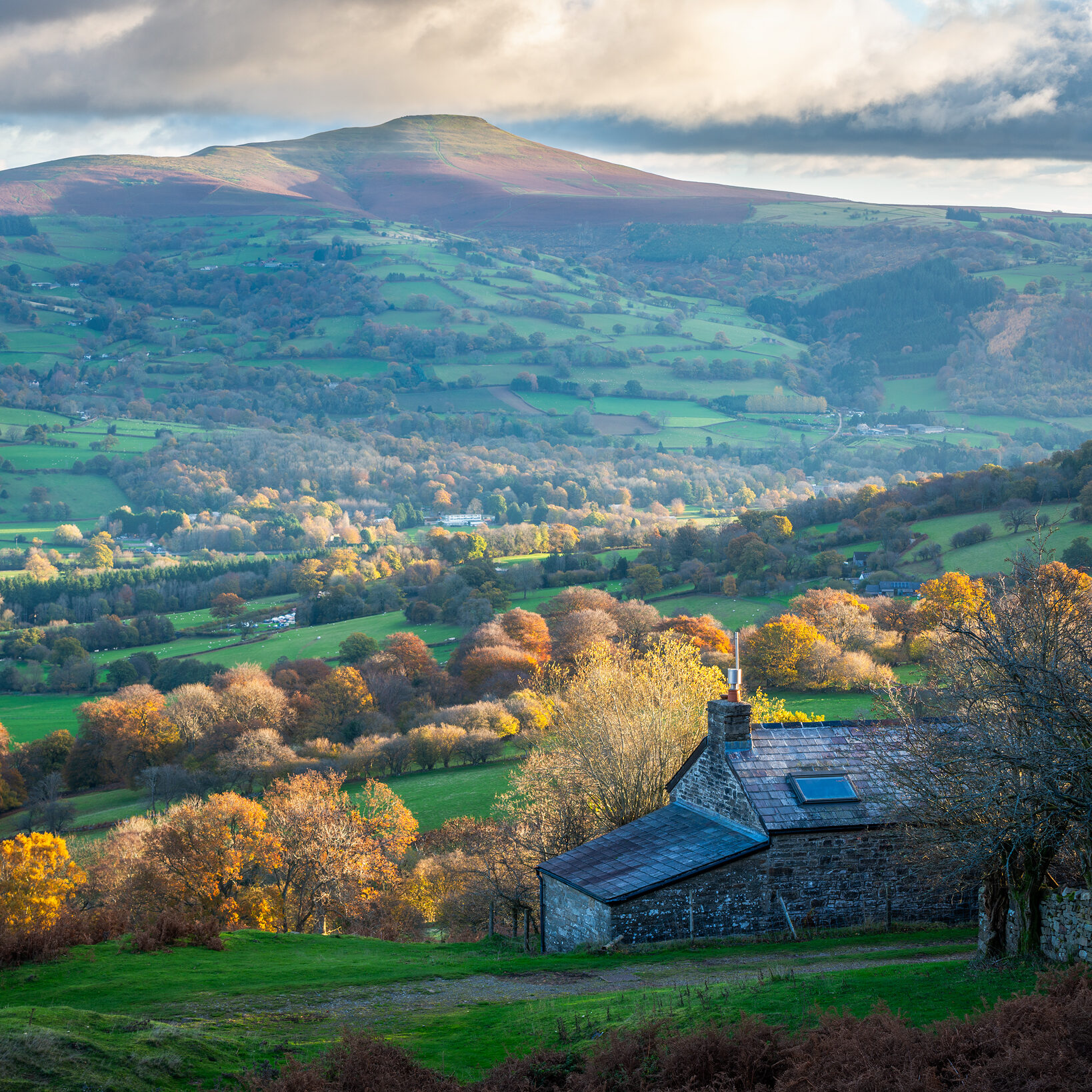 The rising sun sets the autumn landscape of the Brecon Beacons aglow, as well as the cozy town of Crickhowell below Sugar Loaf Mountain.